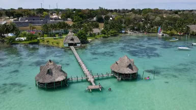 a group of huts on a dock over a body of water with Xelha in the background