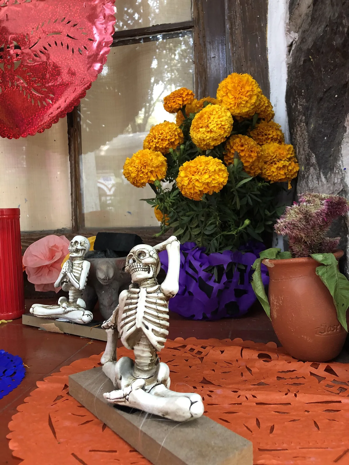 Orange cempasúchil marigolds in a vase beside a small skeleton figure on an ofrenda