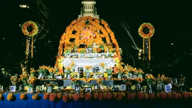 Large lit Día de los Muertos altar at Grand Park with Los Angeles City Hall glowing behind it at night